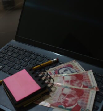 Imágen de una laptop con un blog de notas y billetes de soles peruanos