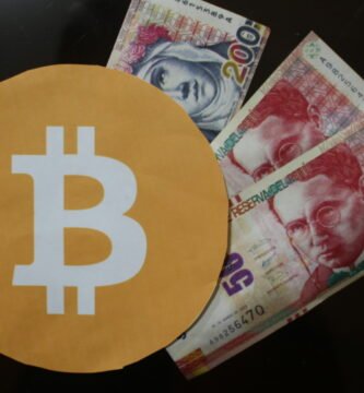 Imágen con el simbolo del bitcoin y billetes de sol peruano en una mesa transparente